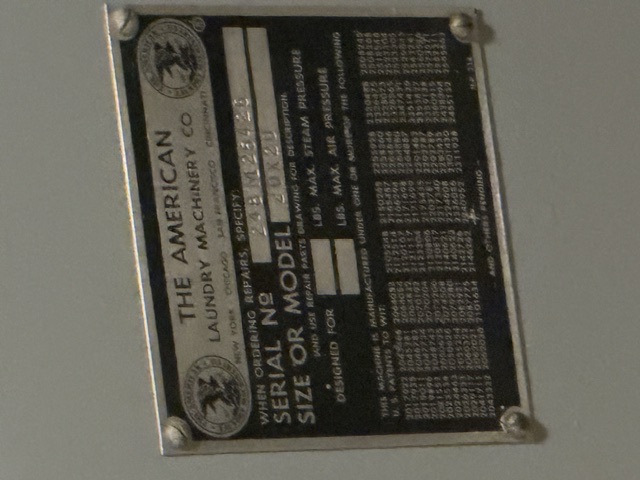 The American Laundry Machinery Co builder's nameplate documented aboard USS Alabama (BB-60) — A metal builder's nameplate reading 'The American Laundry Machinery Co' (New York, Chicago, San Francisco, Cincinnati) with serial number and size/model fields, mounted on laundry equipment aboard USS Alabama.