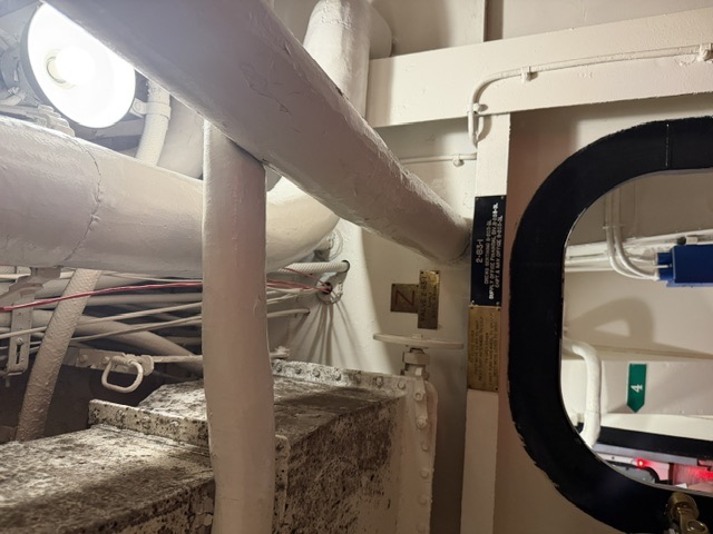 Overhead insulated piping and a lagged ventilation trunk run above a gasketed watertight doorway in a passageway marked with compartment plate 2-63-1 aboard USS Alabama.