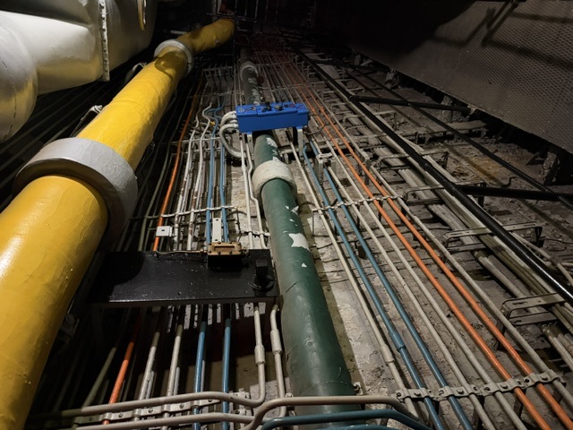 An interior cableway/passageway aboard USS Alabama showing insulated (lagged) overhead piping running above tiered banks of color-coded electrical cabling secured to the bulkhead.