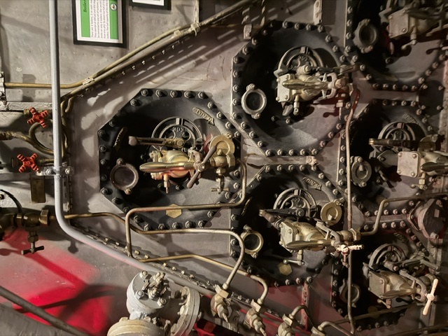 The bolted front casing of a boiler aboard USS Alabama, showing multiple burner air registers and their fuel-oil burner assemblies with a partially visible green museum placard at upper right.