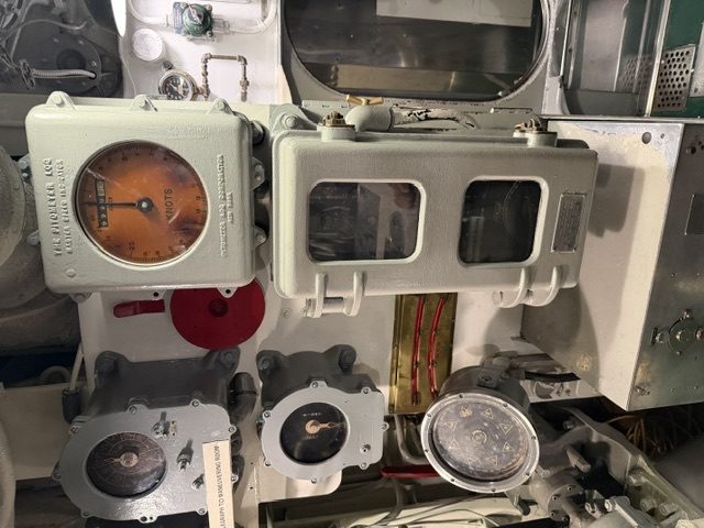 A Pitometer Log Corporation speed indicator reading in knots, mounted with telegraph repeaters and gauges among the control-room instrumentation aboard USS Drum.