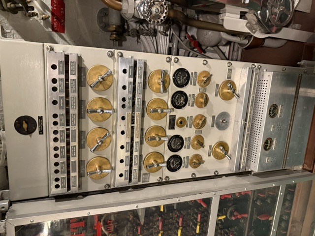 An electrical switchboard aboard USS Drum showing multiple brass rotary switches, labeled circuit indicators, and gauges used to distribute and monitor the submarine's electrical power.
