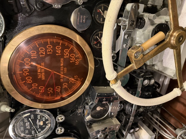 A deep 'Salt Water Depth to Keel' depth gauge graduated 15-165 feet, flanked by a 'Hydraulic Gauge Vents' gauge and other instruments above a canvas-wrapped brass control wheel at the submarine's diving station.