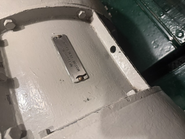 Close-up of the No. 1 Lighting motor-generator set aboard USS Drum, showing its gray-painted casing and a metal identification plate reading "No 1 LIGHTING MOTOR-GENERATOR."