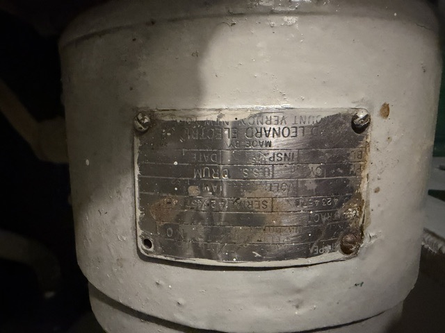 Leonard Electric builder's nameplate documented aboard USS Drum (SS-228) — Close-up of a tarnished brass builder's name plate reading 'U.S.S. Drum' and 'Made by Leonard Electric, Mount Vernon' fastened to a painted cylindrical piece of machinery aboard the submarine.