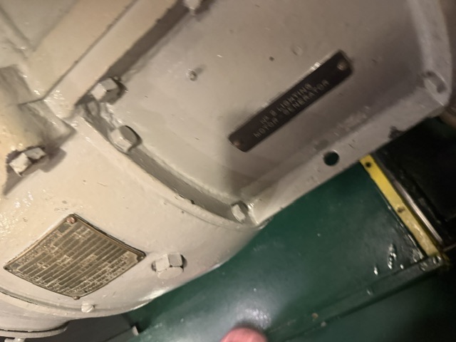 A painted motor-generator set aboard USS Drum, showing a corroded builder's nameplate on the upper housing and a smaller data plate reading 'MOTOR & GENERATOR' on the lower housing.