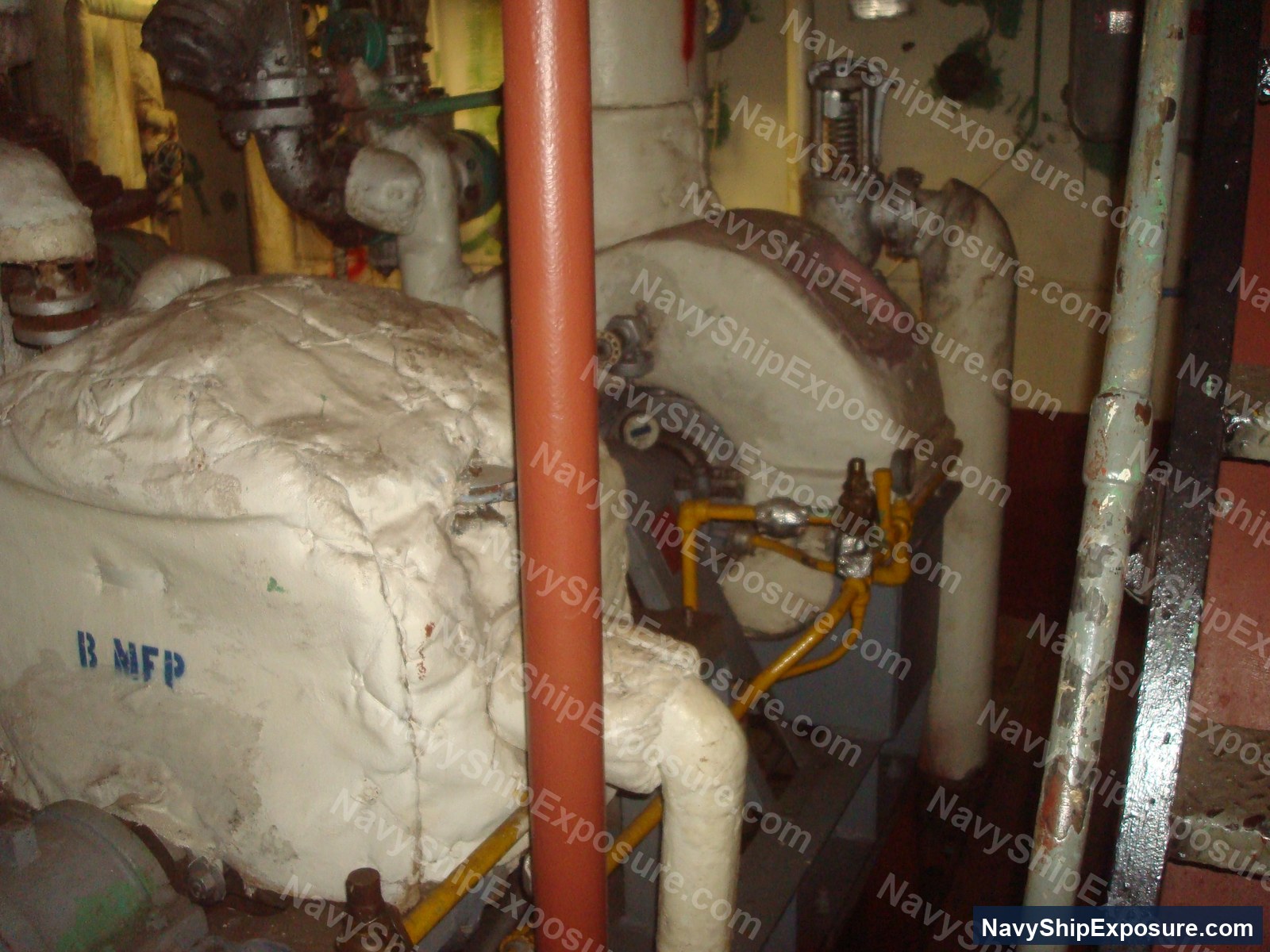 USS Midway — Engine room or machinery space aboard USS Midway showing insulated pipes, valves, and equipment with visible asbestos thermal insulation wrapping, typical of 1945-1992 era naval propulsion systems.