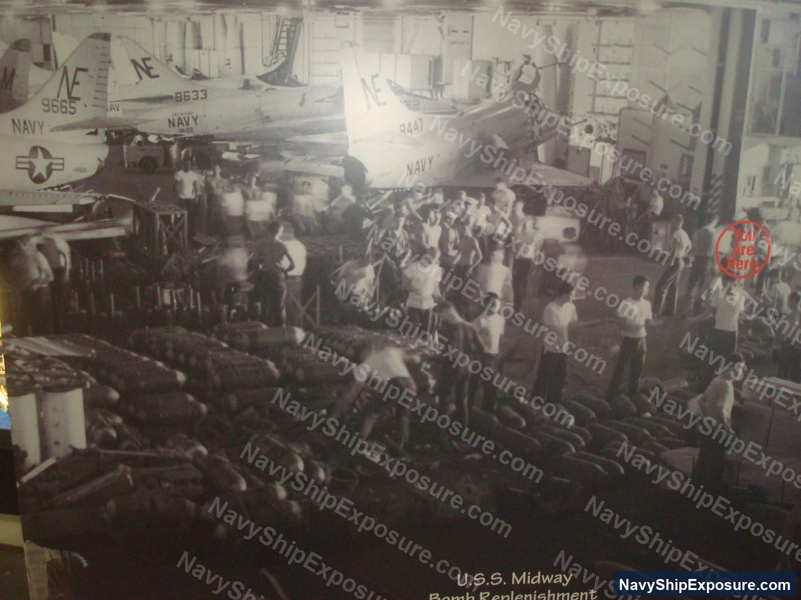 USS Midway — Interior view of USS Midway's bomb replenishment area showing naval personnel working with ordnance and aircraft in the hangar bay during the carrier's operational period.