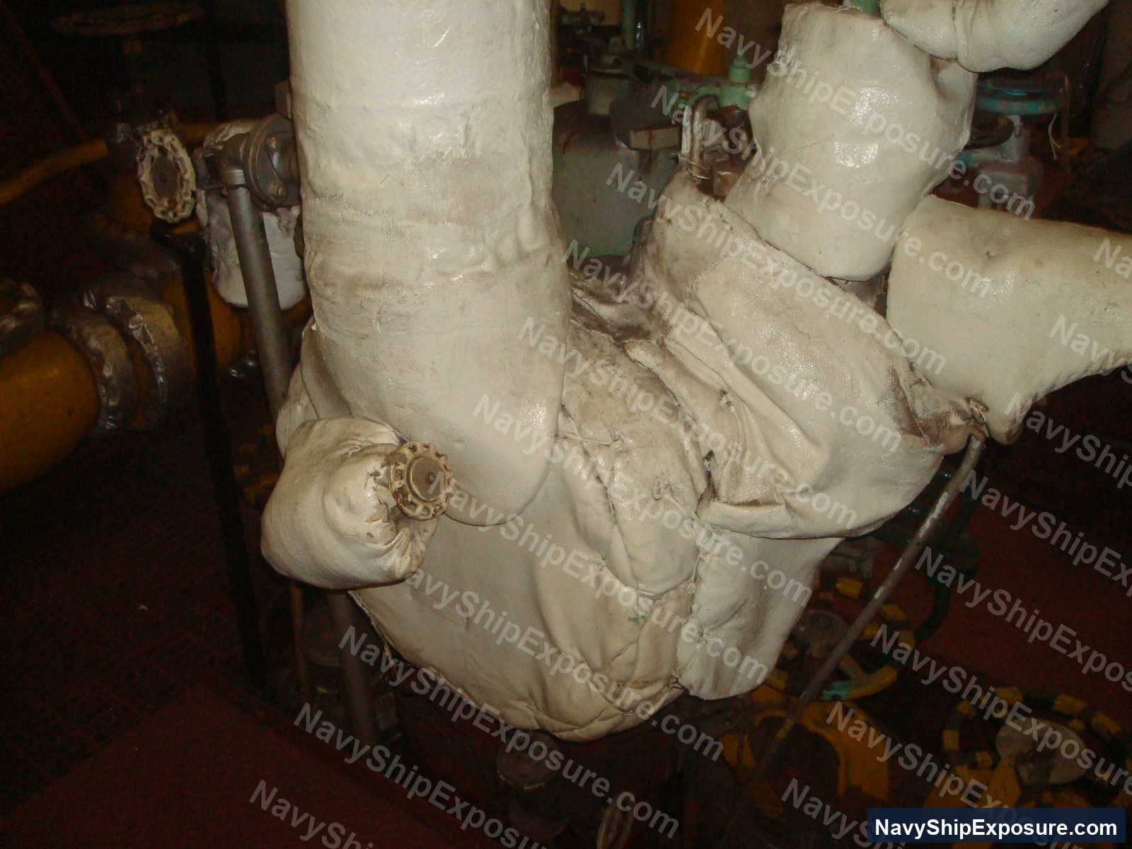 USS Midway — Insulated pipe work in an engine room or machinery space of USS Midway, showing deteriorated asbestos thermal insulation wrapping on large diameter piping and elbow joints.