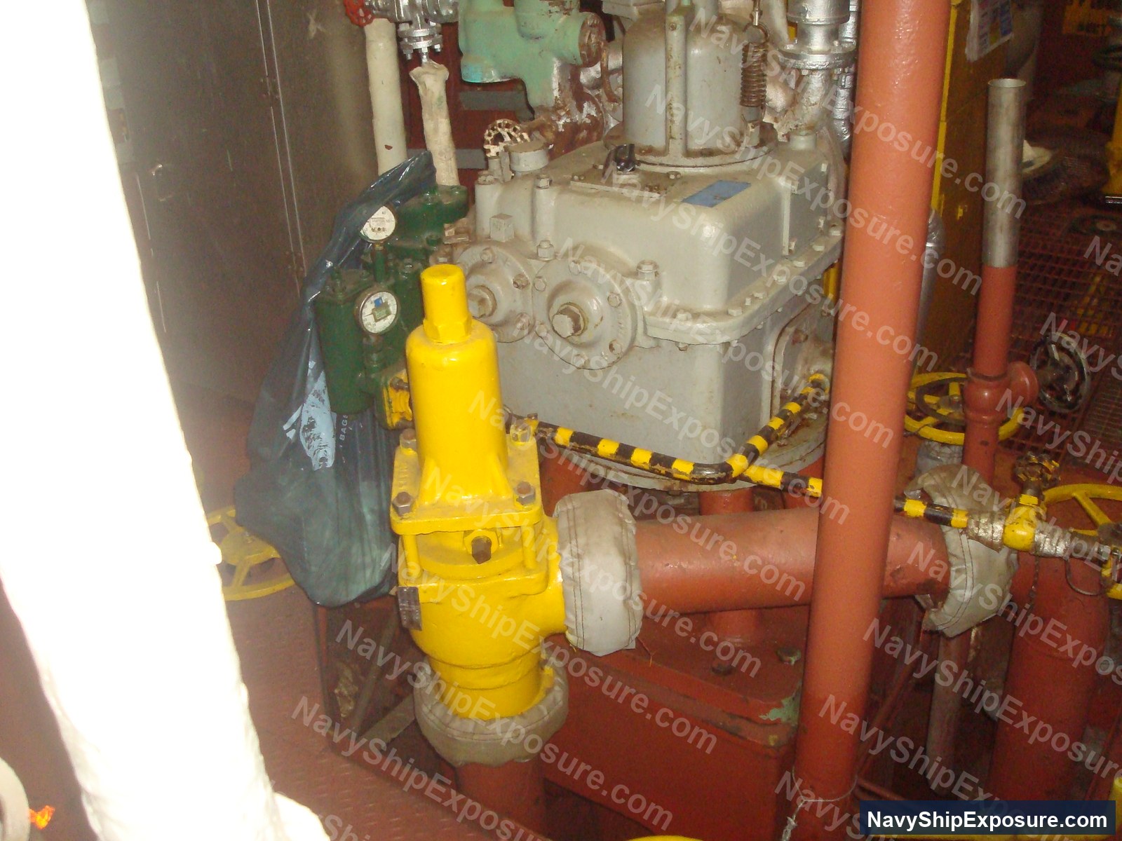 USS Midway — Engine room or machinery space aboard USS Midway showing industrial pump equipment with yellow safety device, red piping, and cream-colored machinery typical of 1940s-1950s naval vessel propulsion systems.