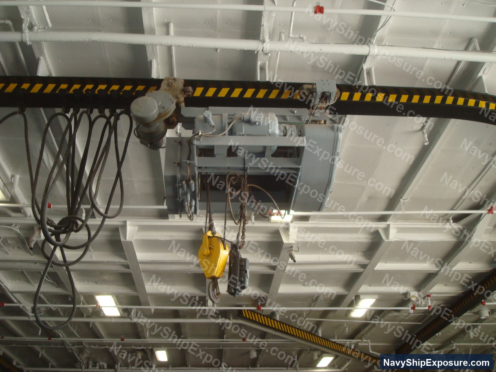 USS Midway — Overhead view of a ship's electric hoist system mounted on an I-beam with motor and chain rigging equipment typical of aircraft carrier machinery spaces.