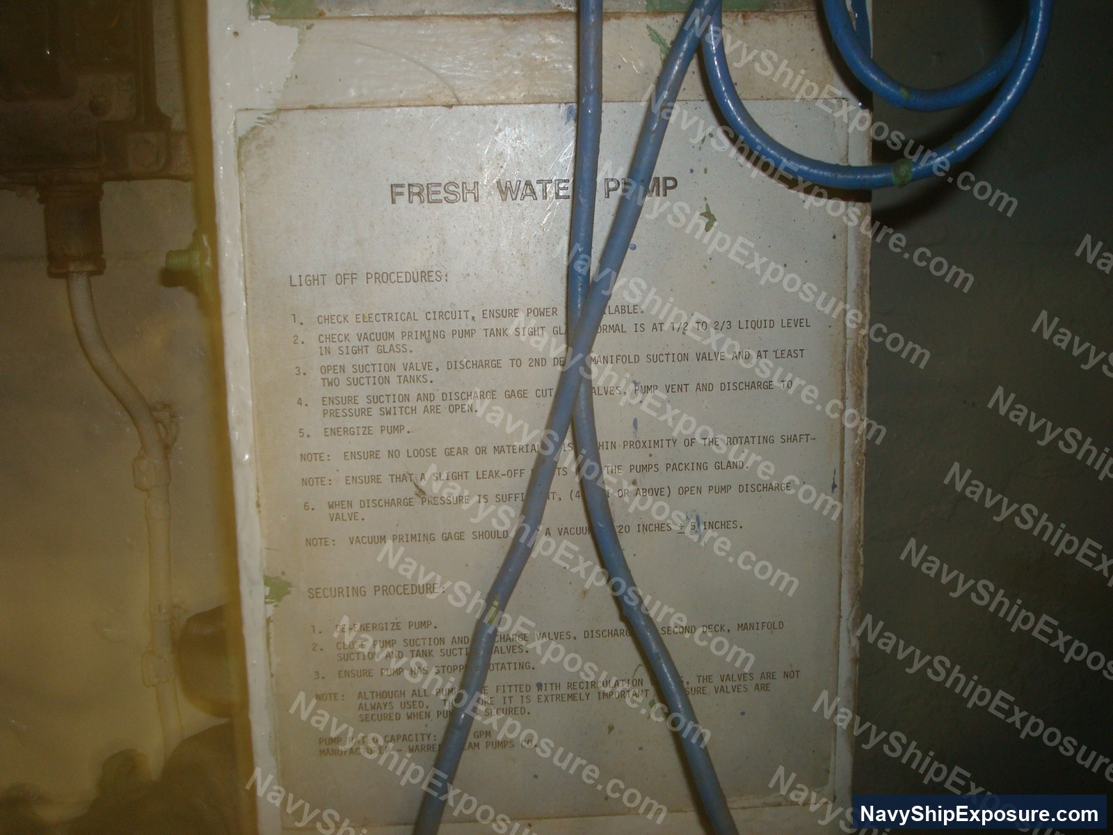 USS Midway — Instruction placard for fresh water pump operations aboard USS Midway, detailing light-off procedures, securing procedures, and pump specifications with blue hoses crossing the laminated label.