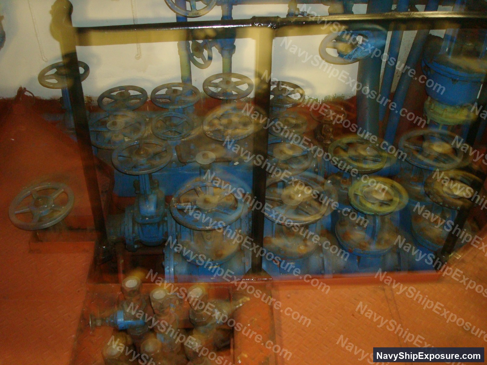 USS Midway — Engine room or machinery space aboard USS Midway showing multiple blue industrial valve assemblies with hand wheels mounted on pipes and equipment, typical of naval propulsion system infrastructure from the 1945-1992 era.