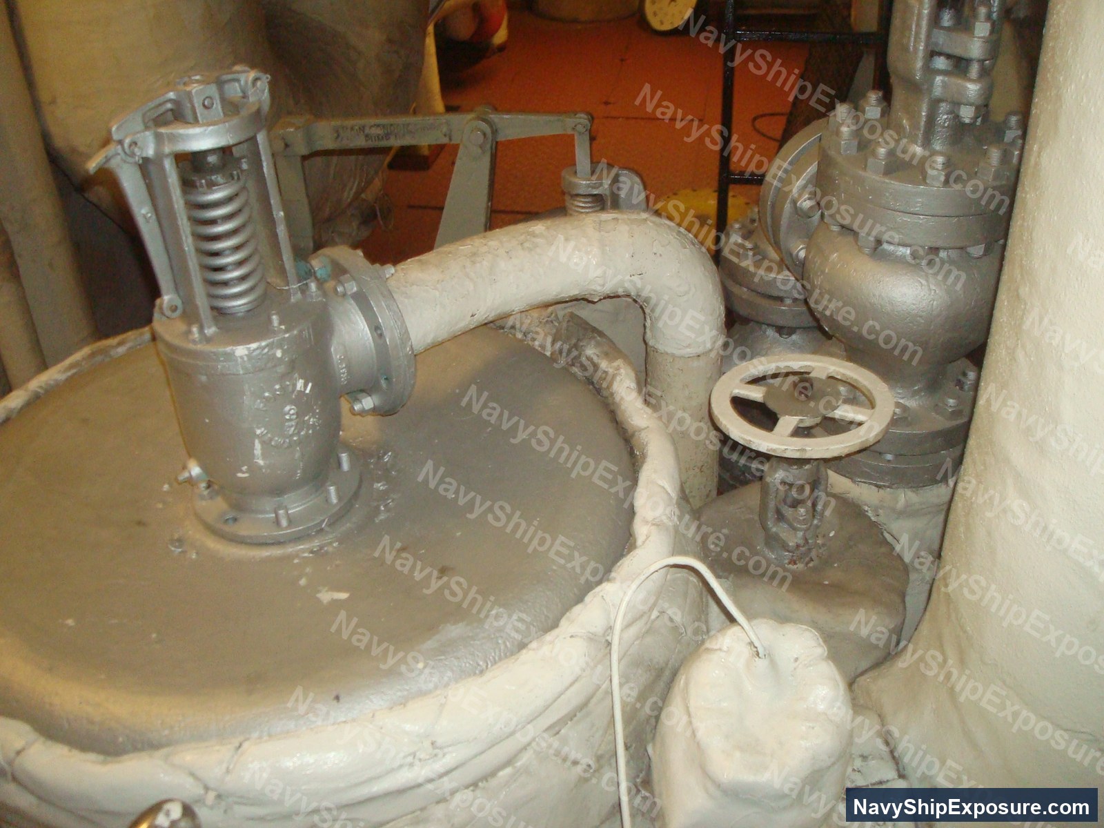 USS Midway — Engine room or machinery space piping assembly with insulated pipes, valves, and mechanical equipment typical of USS Midway's steam propulsion system, showing deteriorated thermal insulation consistent with asbestos-containing materials used on naval vessels of that era.