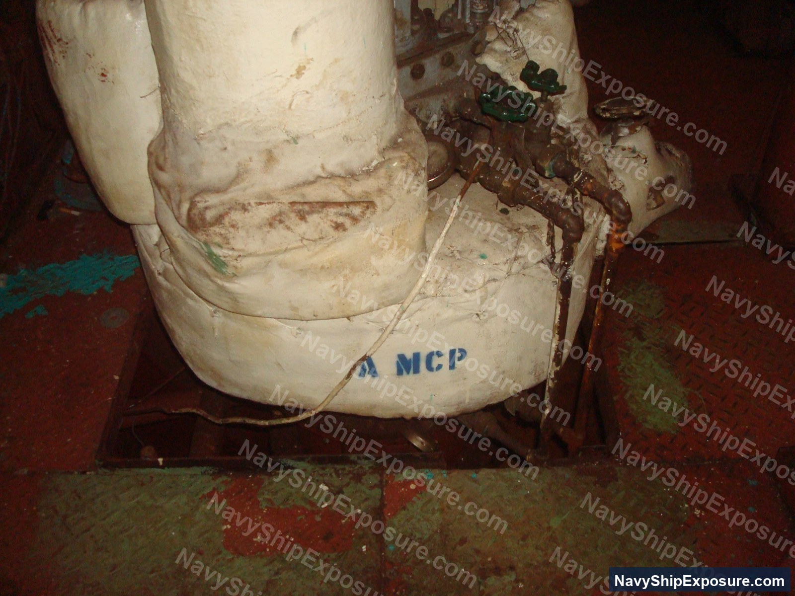 USS Midway — Close-up photograph of a large cylindrical pipe or vessel component labeled 'MCP' in an engine room or machinery space aboard USS Midway, showing deteriorated insulation material and corrosion typical of naval engineering spaces from the Cold War era.