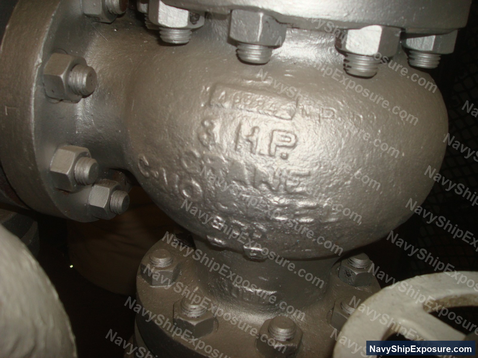 USS Midway — Close-up photograph of a spherical pressure vessel or accumulator with multiple threaded ports and hex-head fasteners, likely from the USS Midway's engineering plant or steam system.