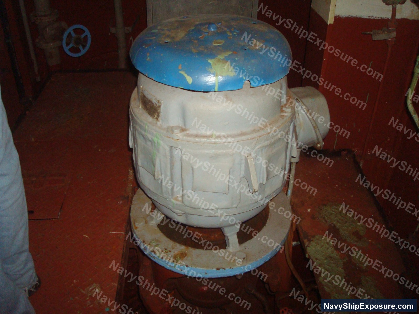 USS Midway — An electric motor with a blue top mounted on a base in an engine room or machinery space of USS Midway, showing deteriorated condition and potential asbestos-containing insulation materials typical of 1940s-era naval vessels.