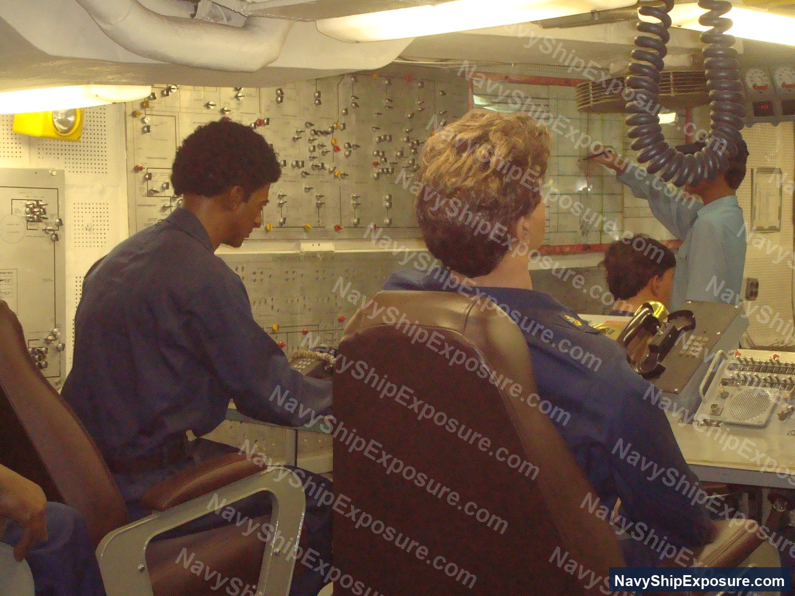 USS Midway — Engine room or machinery control space aboard USS Midway showing electrical control panels, instrumentation boards, and crew members operating engineering systems typical of 1940s-1960s naval vessels.