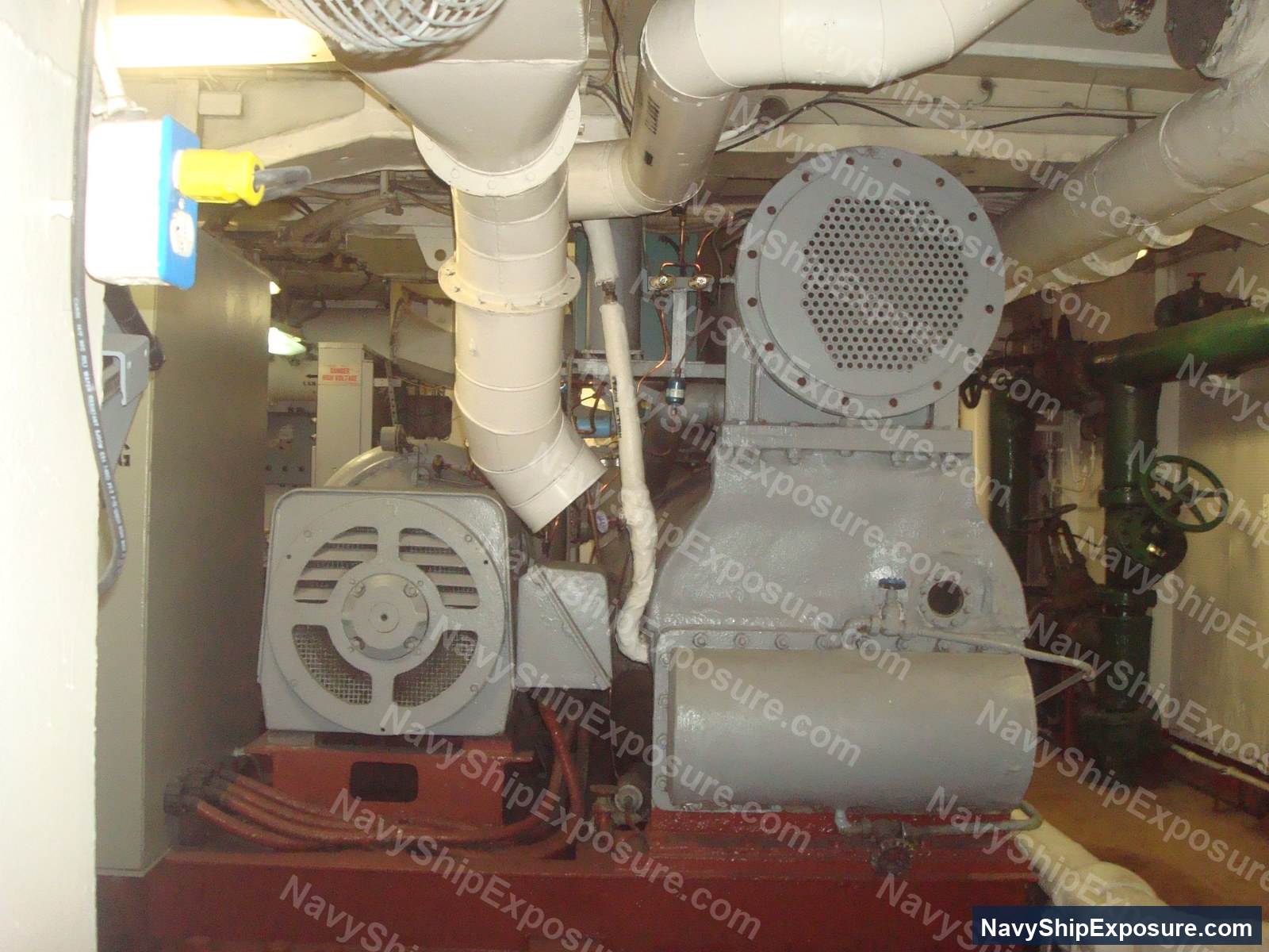USS Midway — Engine room or machinery space aboard USS Midway showing electrical motors, large cylindrical equipment (likely condensers or heat exchangers), white piping systems, and a red-painted deck typical of naval engineering spaces from the 1940s-1992 era.