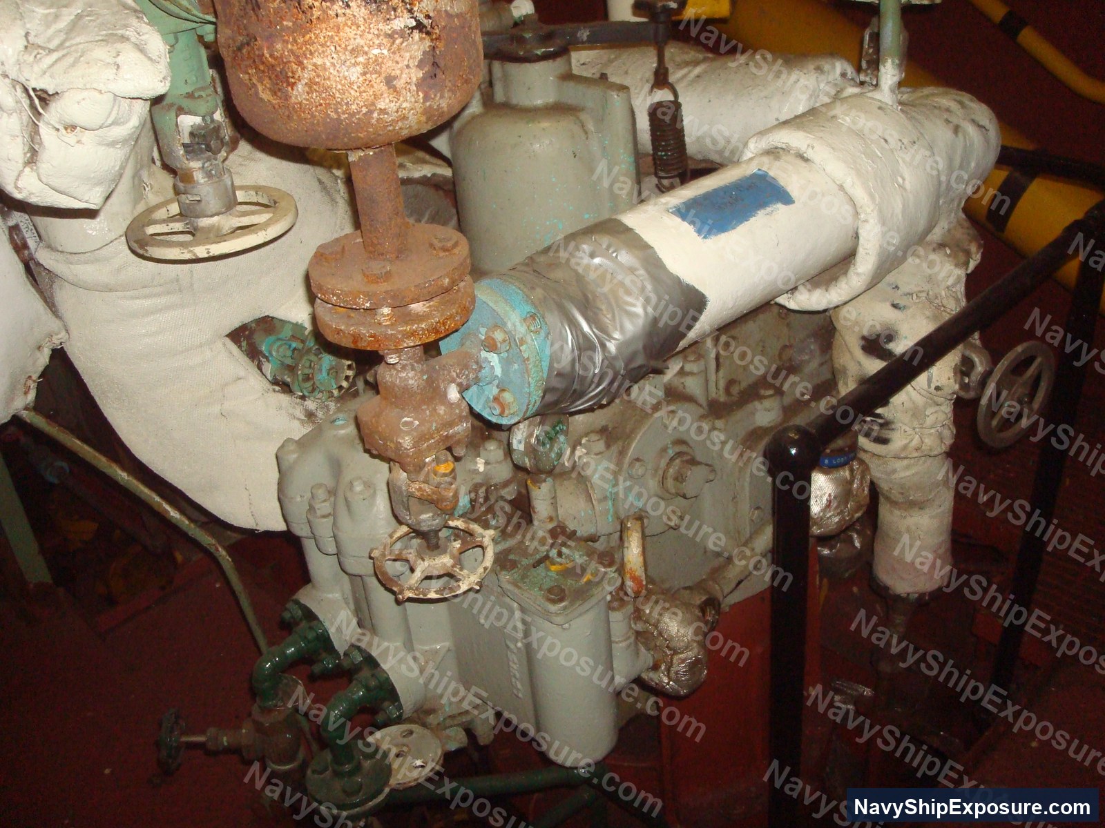 USS Midway — Engine room or machinery space equipment from USS Midway showing deteriorated piping, insulation wrapping, valves, and corroded metal components typical of naval propulsion systems that historically contained asbestos materials.